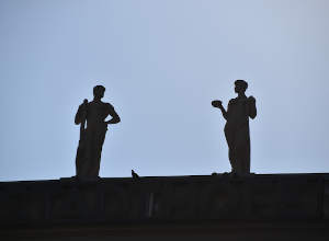 Zwei Statuen vor blauem Himmel schauen sich an.