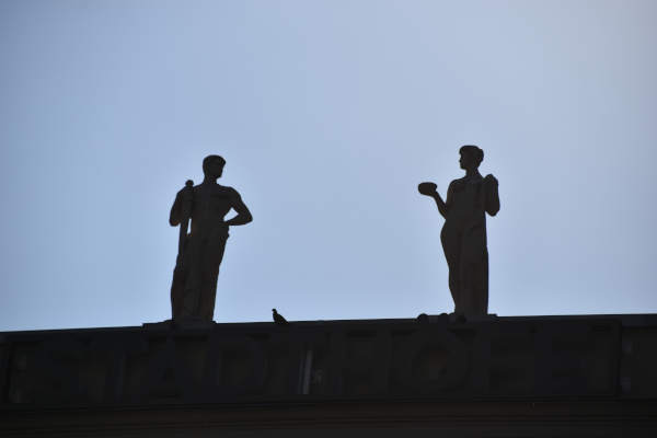 Zwei Statuen vor blauem Himmel schauen sich an.